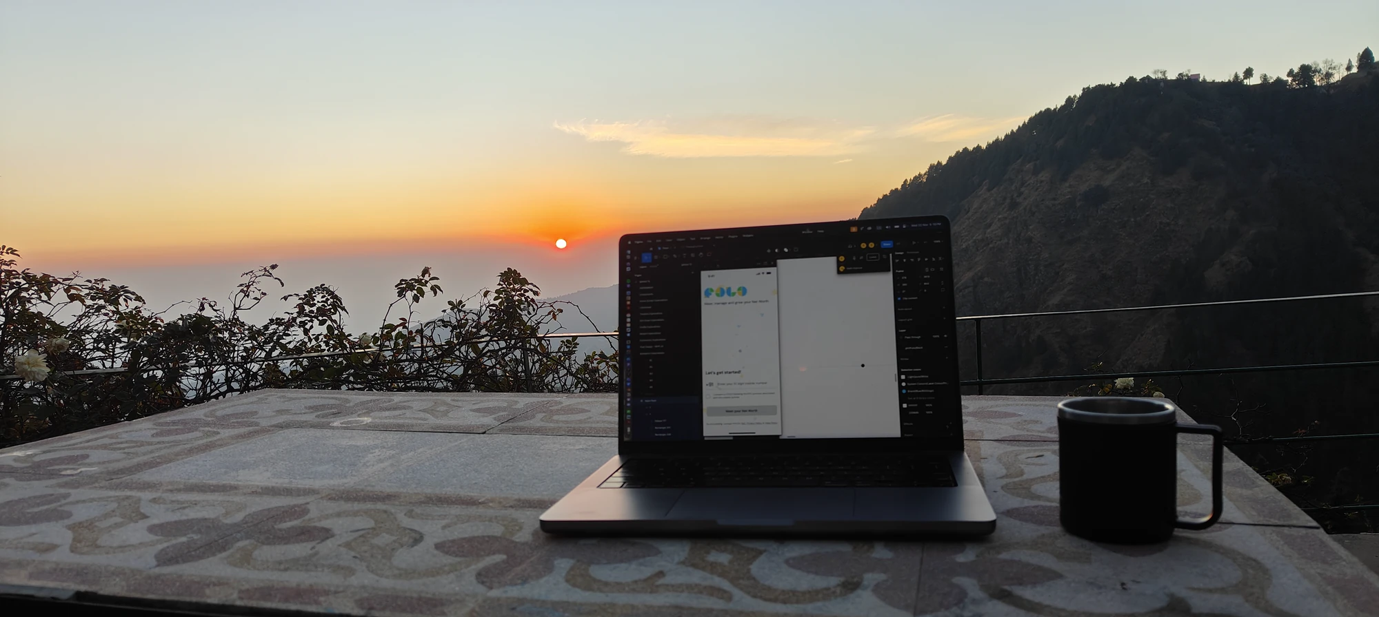 A laptop open to early FOLO design screens on a terrace table at sunrise.